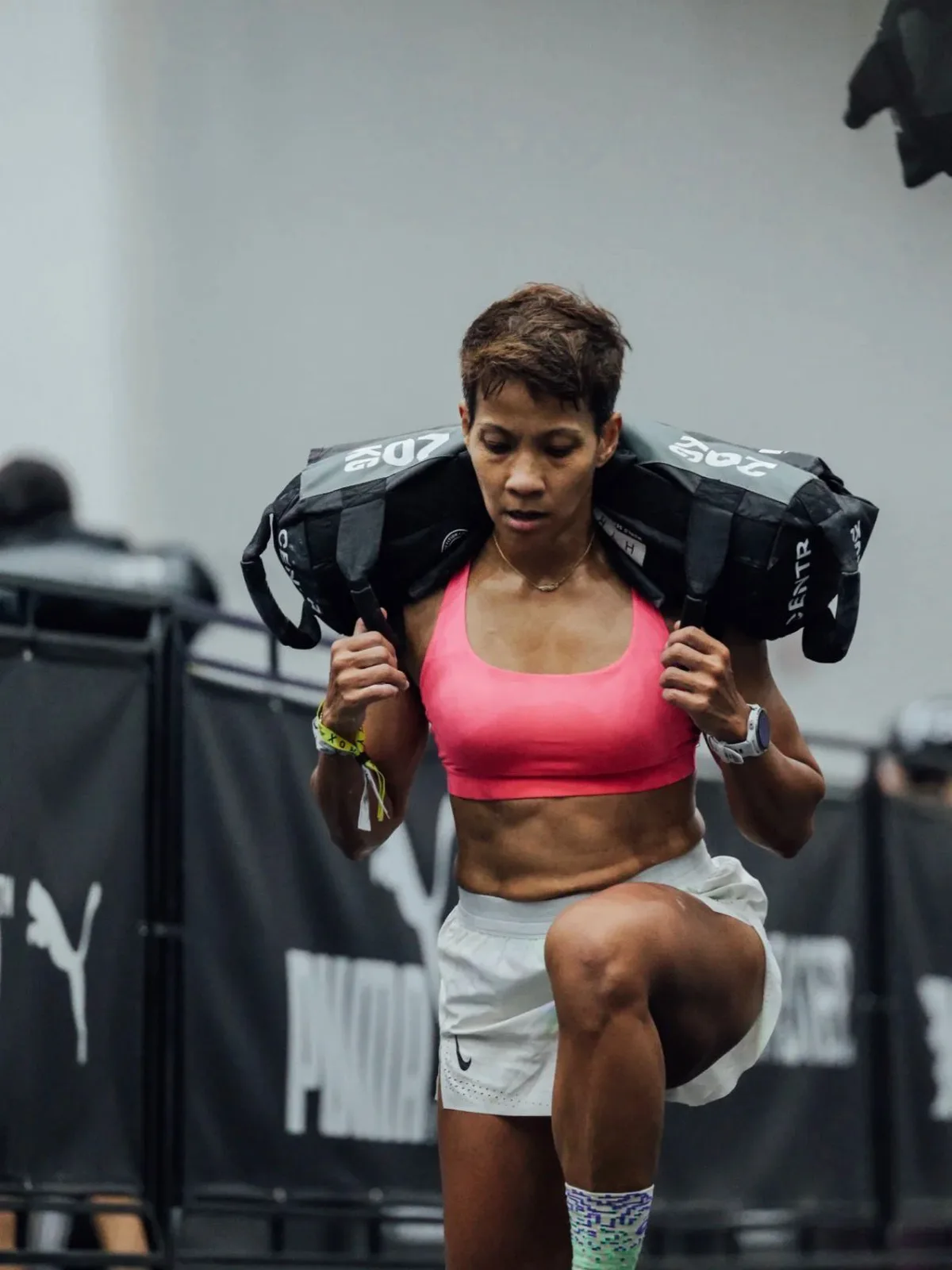 Elly mid-sandbag-carry at a HYROX race, 18 international Over-40 podium finishes, most recently 2nd place