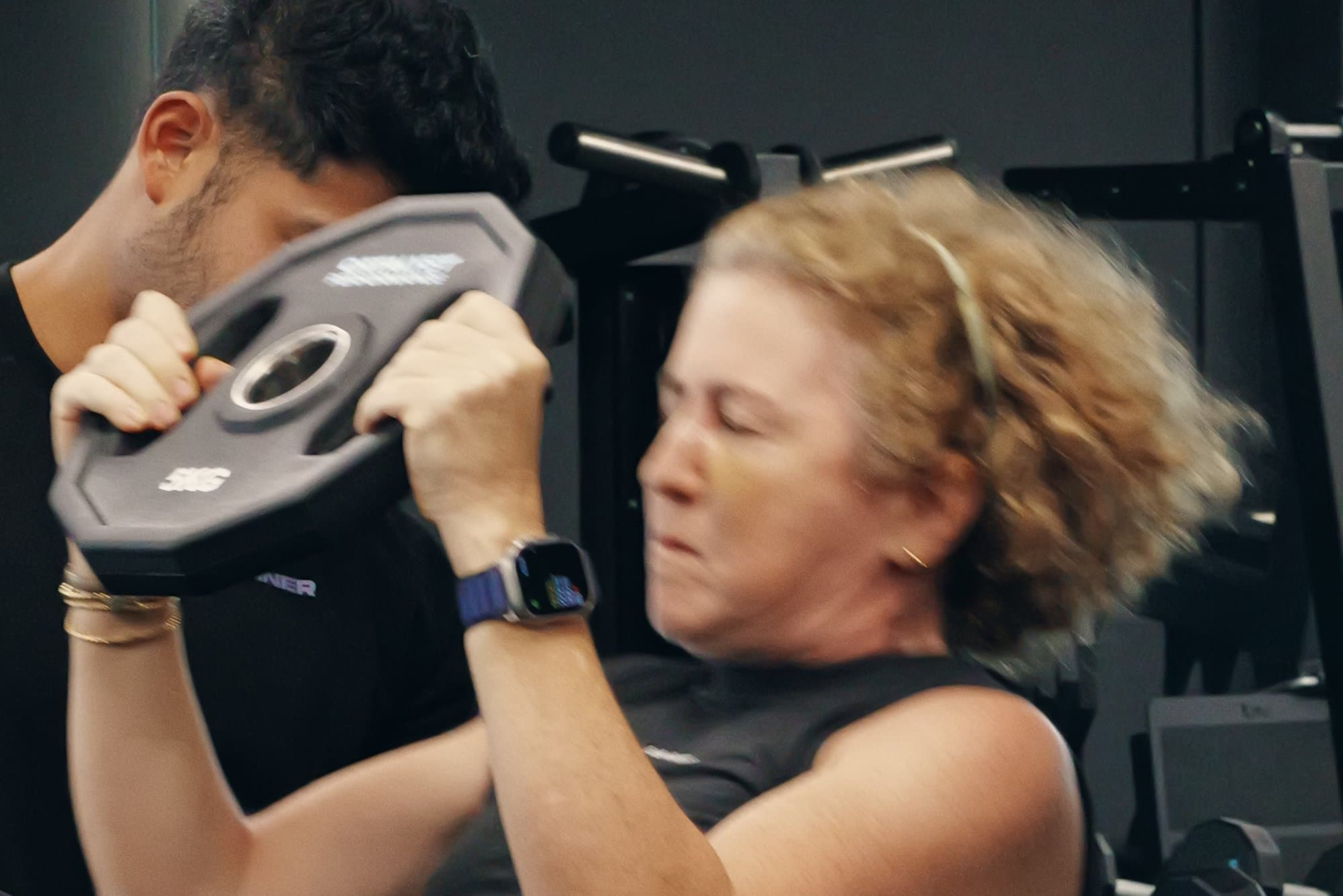 A mature female member doing a weight-plate press with a coach spotting, Catalyst Performance, Singapore CBD personal training studio