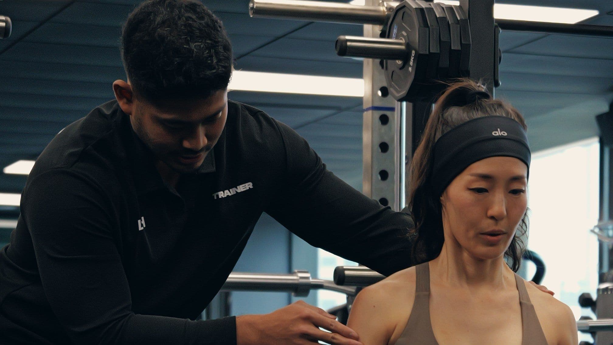 A coach spotting a client's shoulder mid-set during a supervised resistance training session