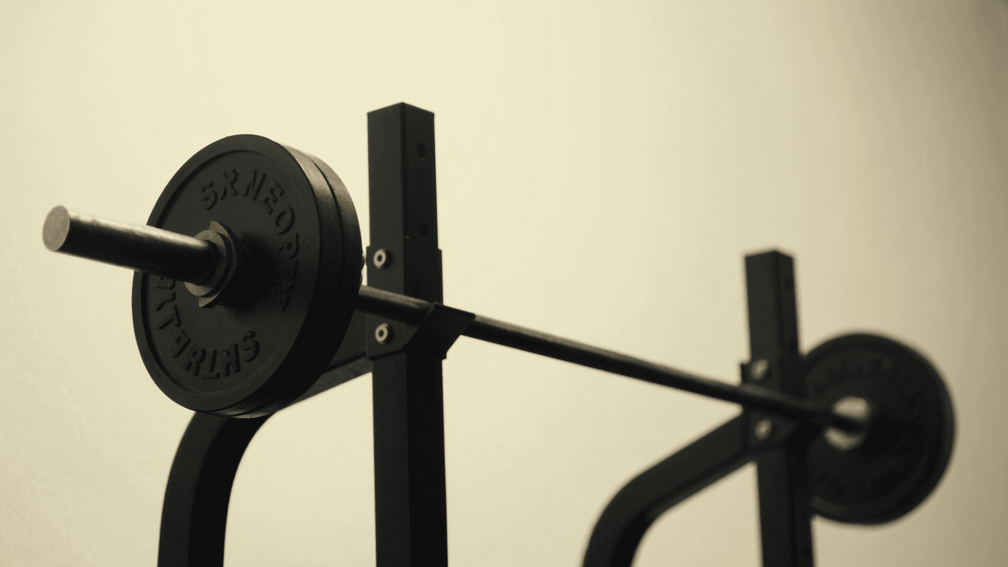 Close-up of a loaded barbell on a rack in a warm-lit private training studio, no person visible