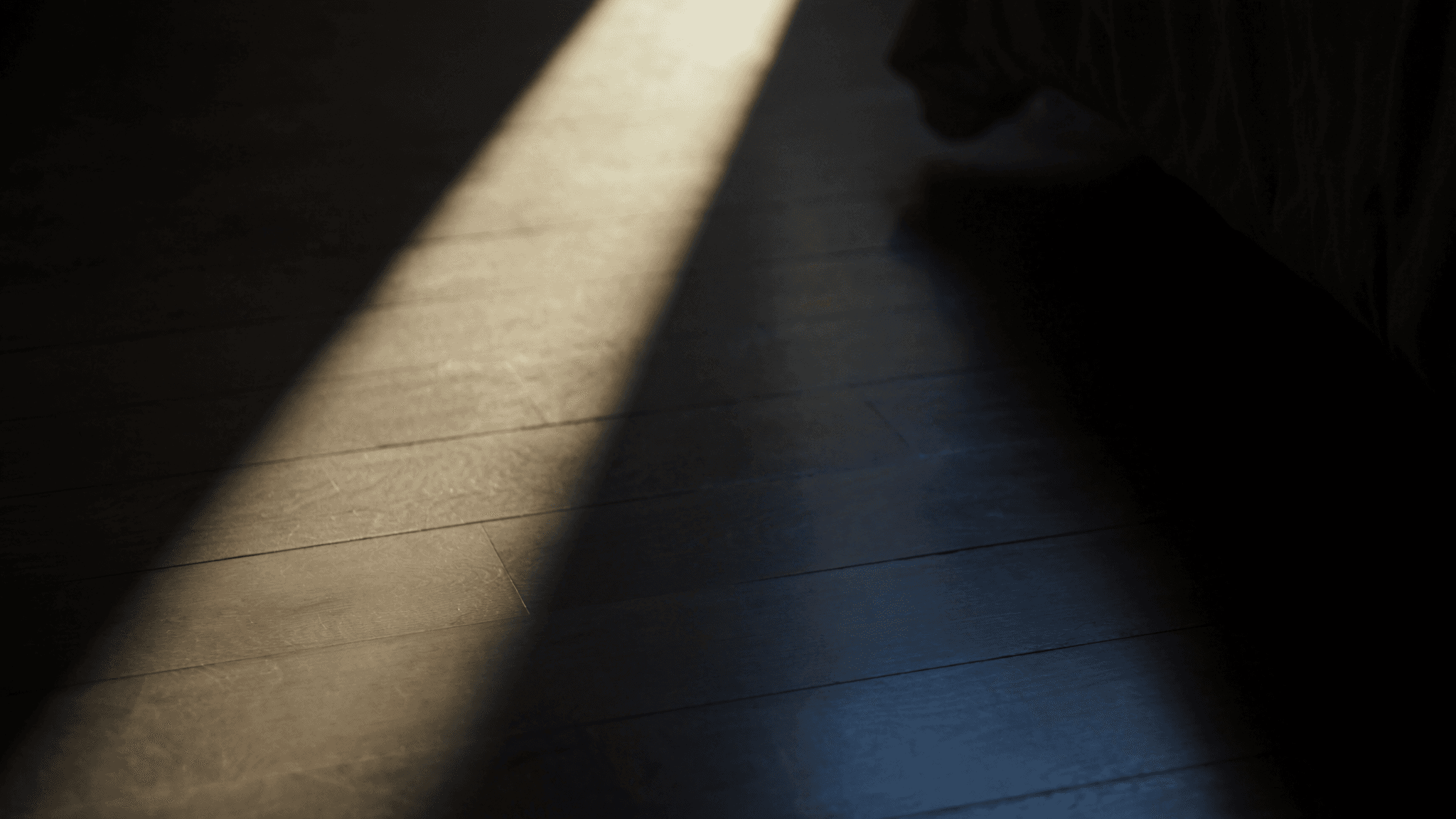 A shaft of early-morning sunlight across a dark wooden bedroom floor, evoking the first painful step of plantar fasciitis