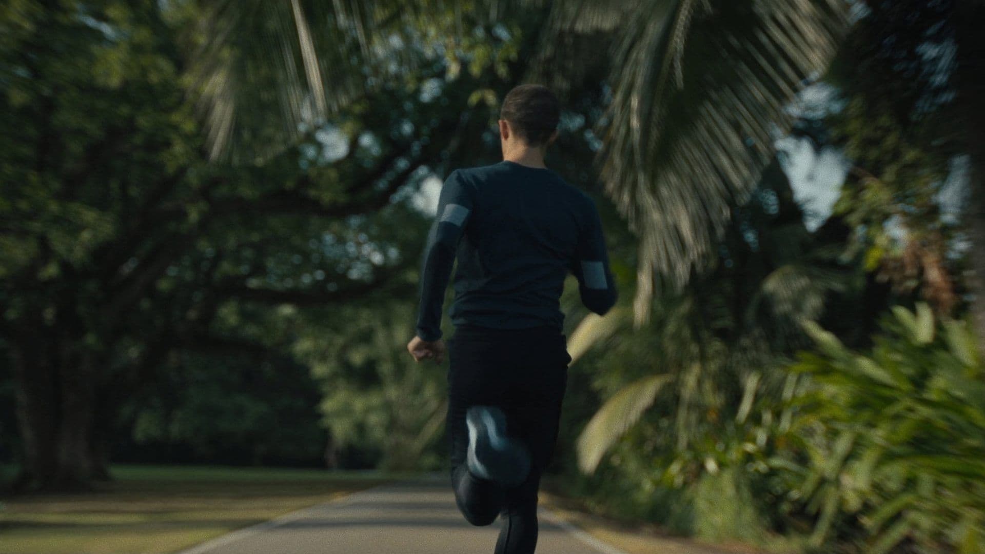 A runner from behind mid-stride on a tree-lined Park Connector path in Singapore at early morning golden hour, lush tropical canopy overhead