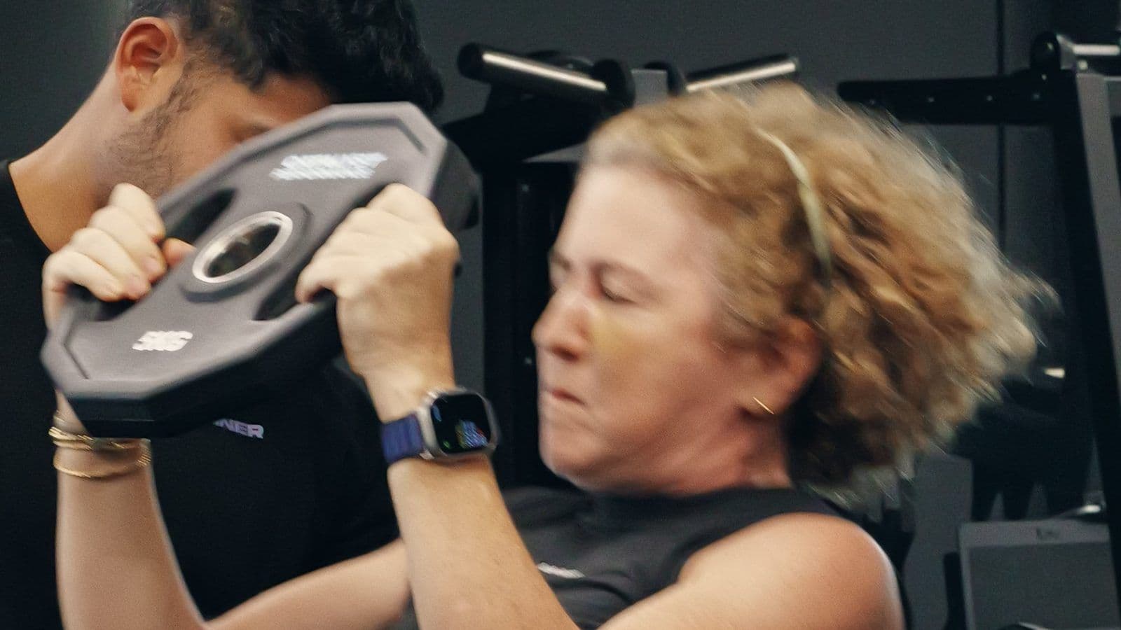 An older woman presses a weight plate under coaching at Catalyst Performance in Singapore