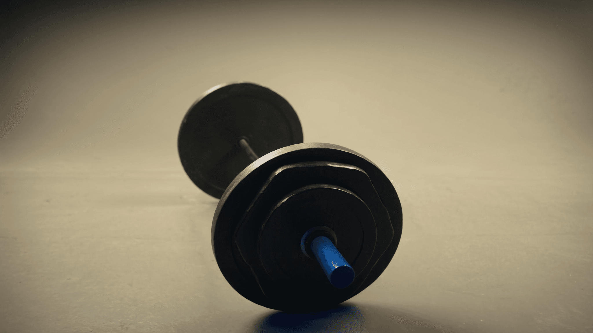 A loaded weight bar with iron plates on a warm studio floor in soft directional light