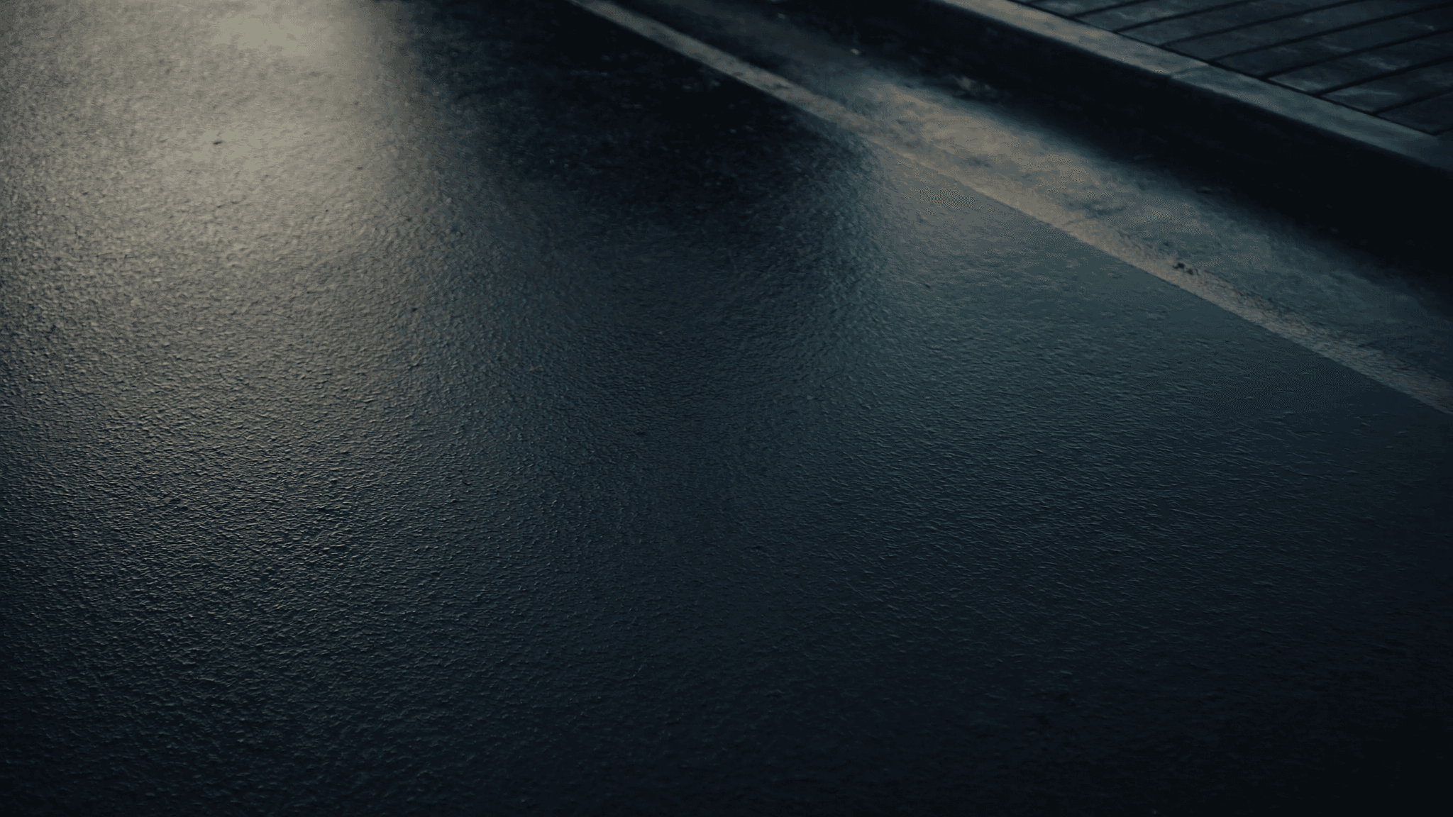 Wet asphalt road surface at dawn with a faint edge line, the impact surface runners train on
