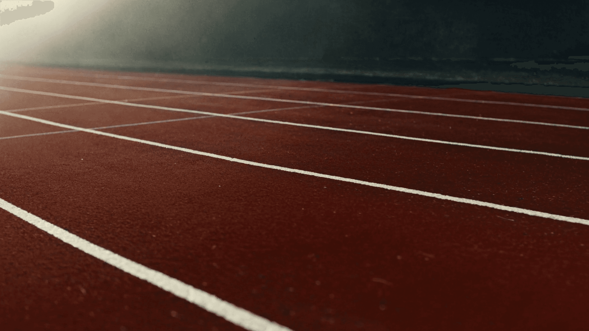 An empty red tartan running track with white lane lines in soft early-morning light