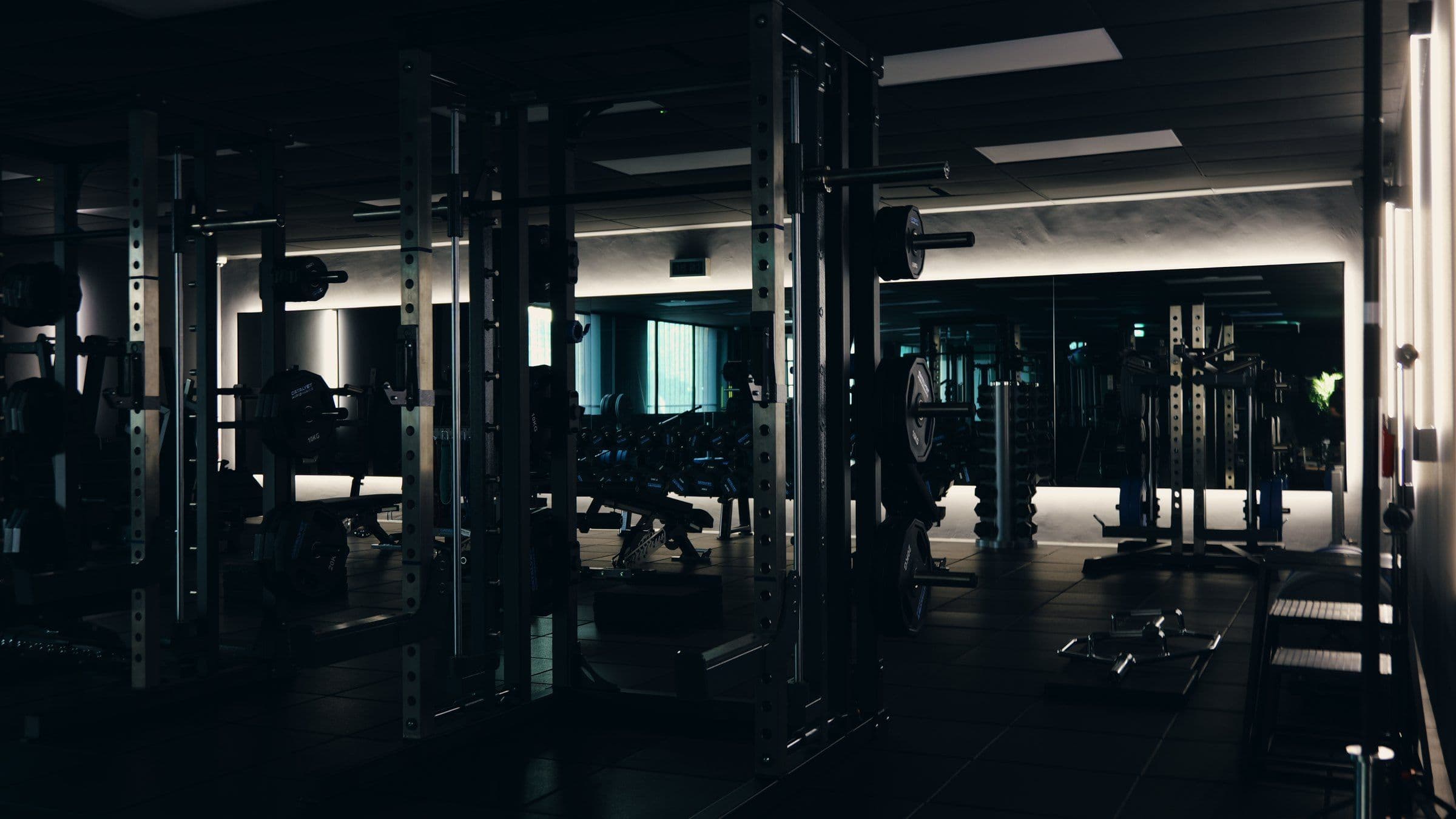 An empty personal training studio in Singapore's CBD, with power racks and loaded barbells in low light