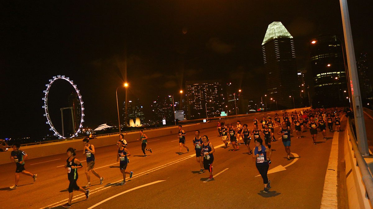 Runners on the course at night during the Sundown Marathon, with the city skyline behind